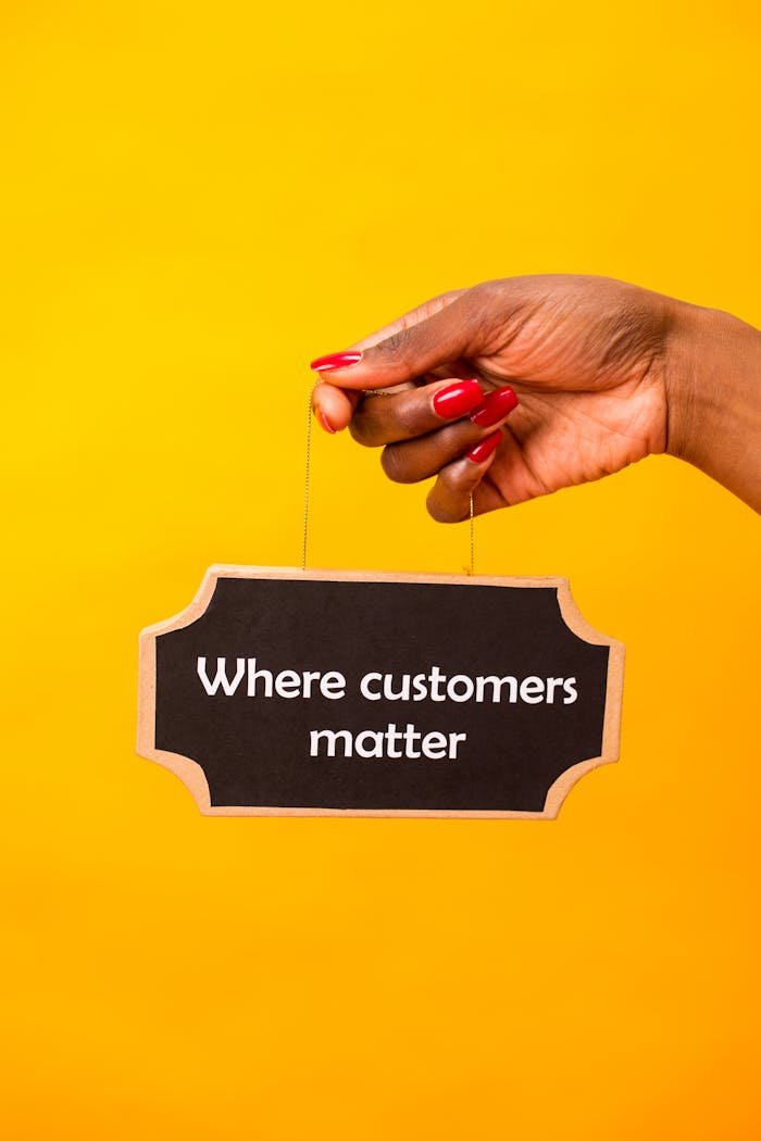 Hand holding a sign with Where customers matter on a vibrant yellow backdrop.